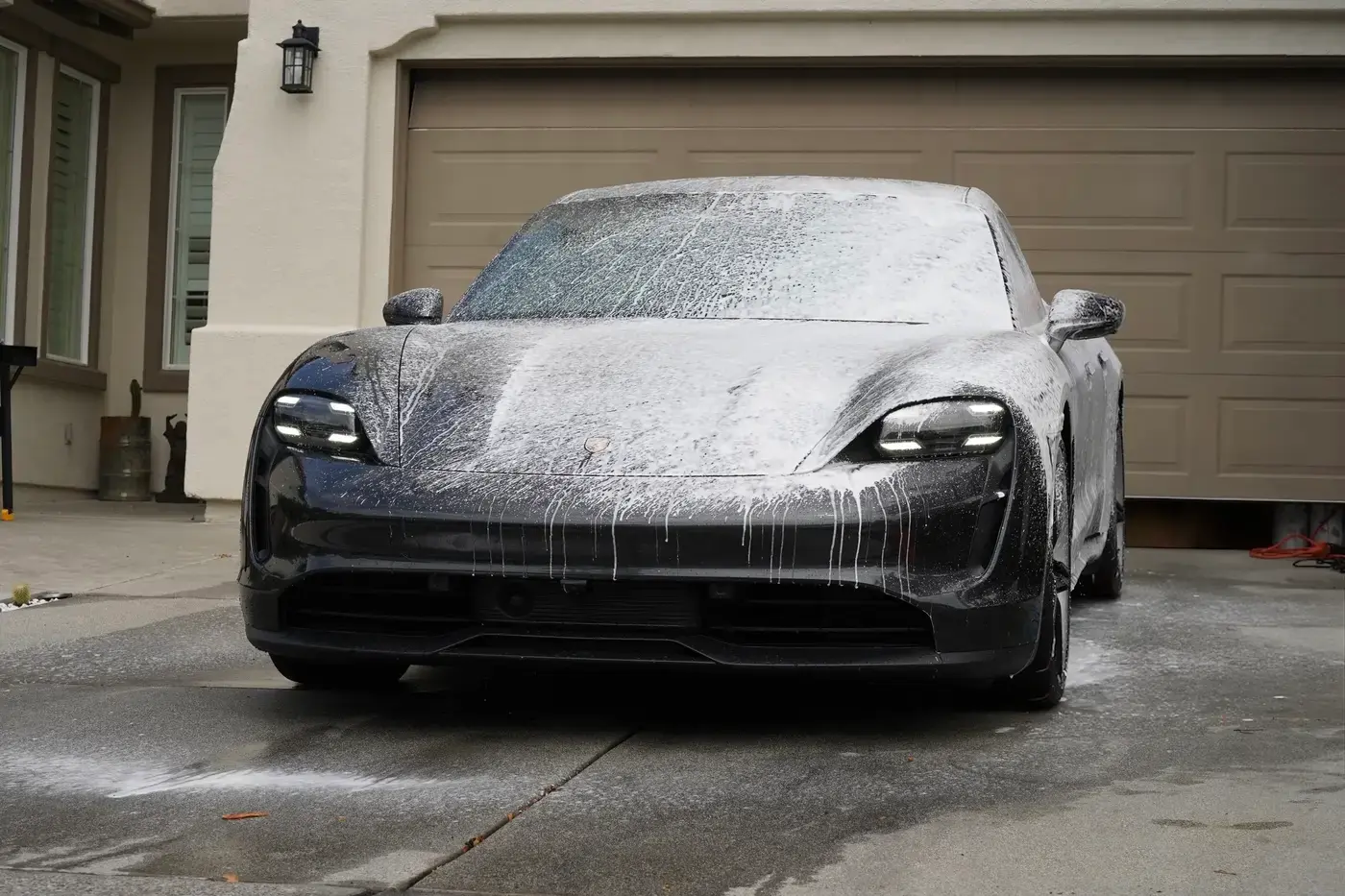 Porsche Taycan covered in foam during a maintenance wash in a client driveway